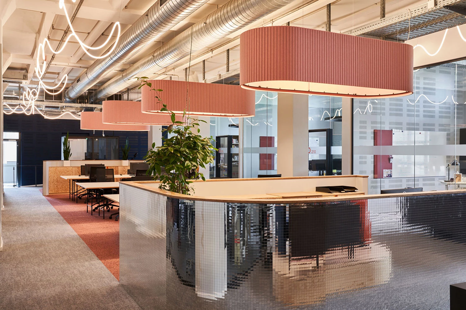 Workstations of the Banijay media company. The large orange acoustic luminaires are striking, providing both area-wide illumination above the workstations and improving the room acoustics.