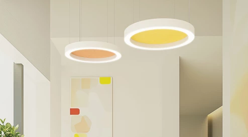 Duas luminárias pendentes redondas brancas com inserção de material acústico colorido, uma em amarelo e outra em laranja, para uma óptima acústica ambiente.
