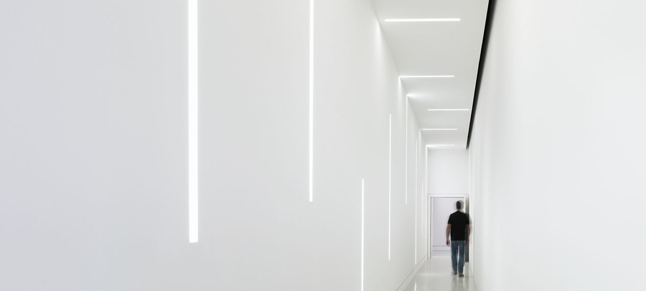 De subtiles lignes lumineuses LED dans un couloir. L'éclairage est monté au mur et au plafond et relié par un connecteur.