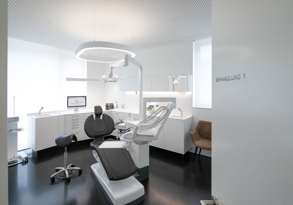 A slim, white pendant light provides precise, glare-free light in the treatment room of a dental practice.