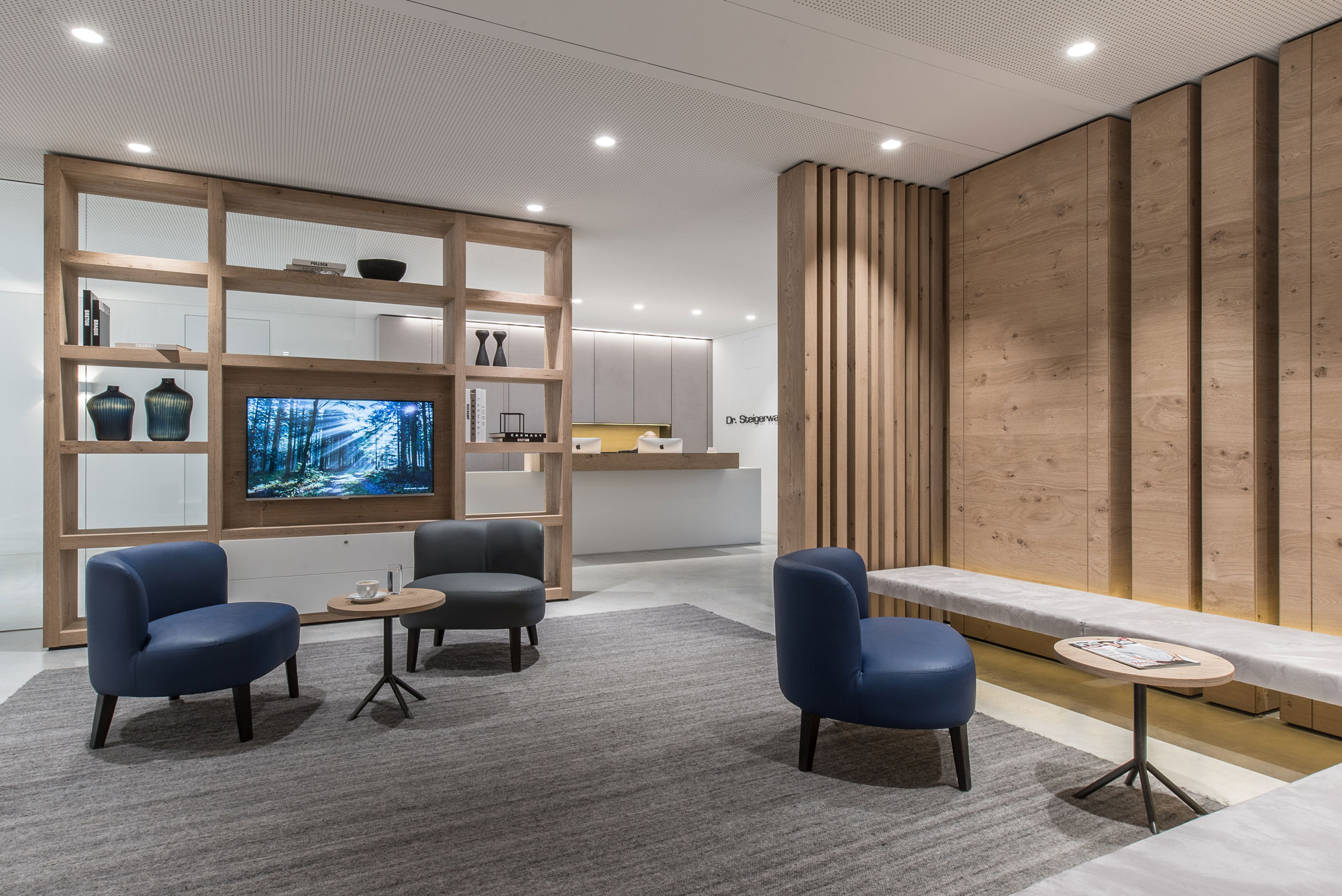 Las discretas luminarias focales empotradas en el techo proporcionan una luz uniforme y sin reflejos y crean un ambiente agradable en la sala de espera de un consultorio médico.